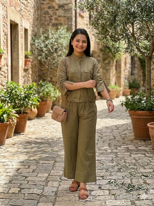 Woman in a mud brown outfit standing on a stone path with potted plants and stone walls in the background