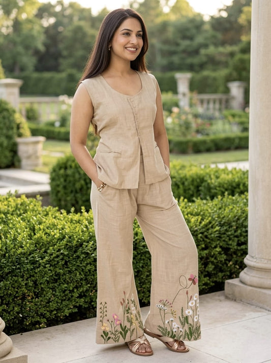 Woman in beige outfit with floral embroidery standing in a garden.