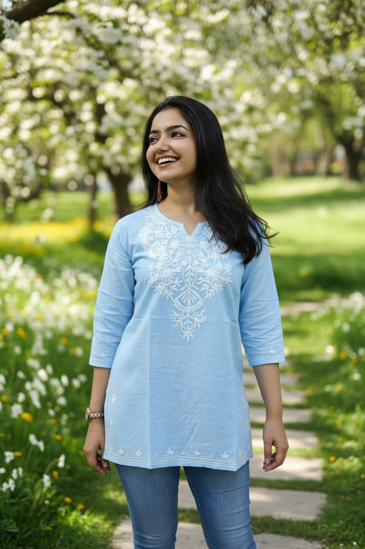 Woman wearing a light blue embroidered top against a pink background