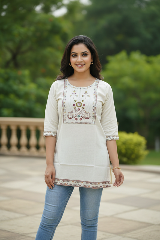 Woman wearing a cream-colored embroidered top with blue jeans outdoors.